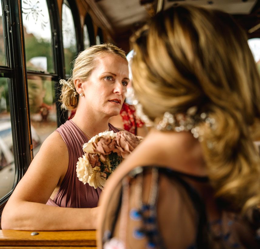 Wedding party members having a conversation inside a vintage trolley with wooden interior details.