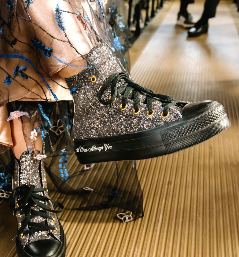 A close-up of sparkly black Converse sneakers worn with a floral dress.