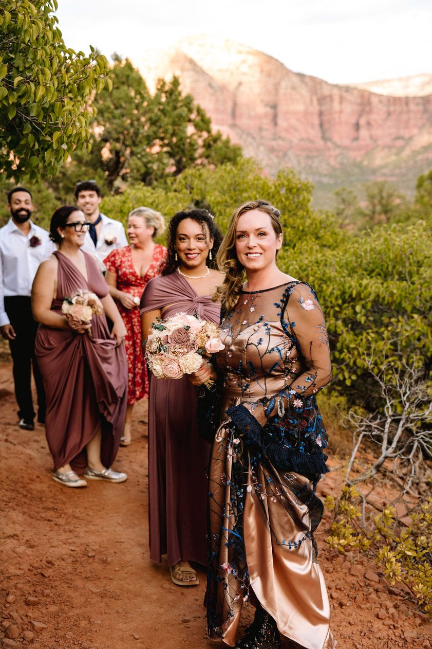 A wedding party posing on a scenic desert trail with Sedona red rock mountains in the background.