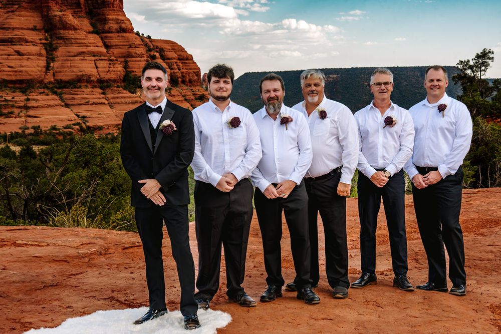 Wedding party poses against stunning red rock formations in Sedona with groomsmen wearing white shirts and black pants.