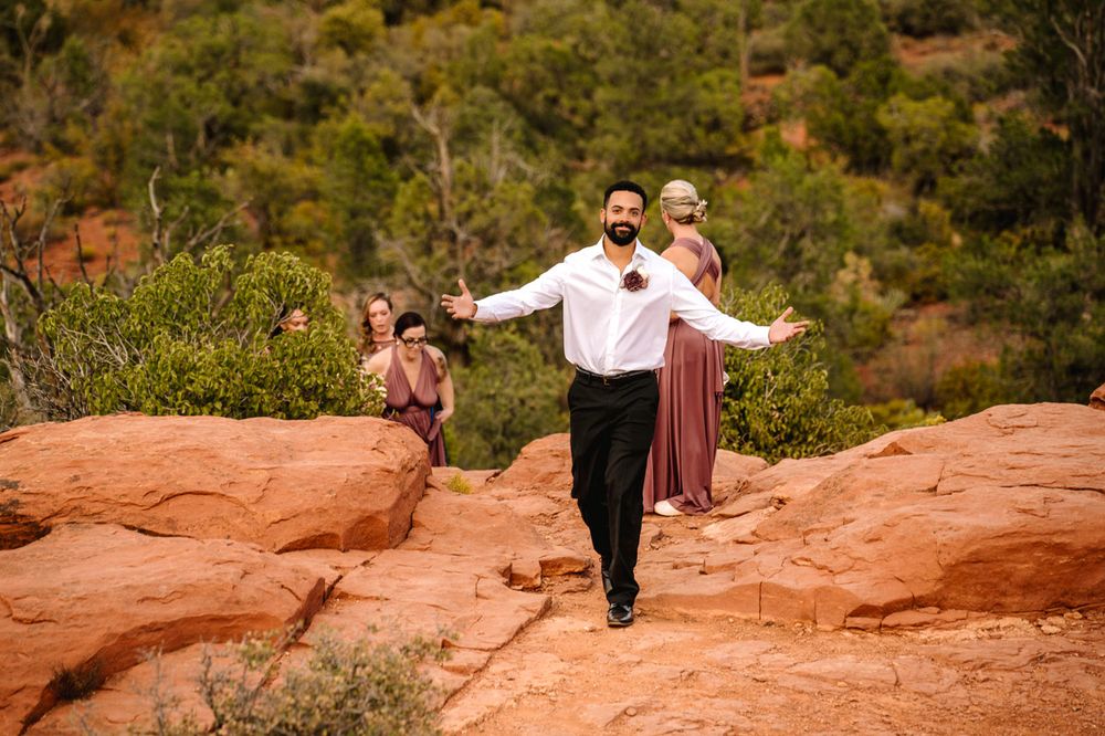 Couple dances joyfully on Sedona red rocks with scenic desert landscape in background.