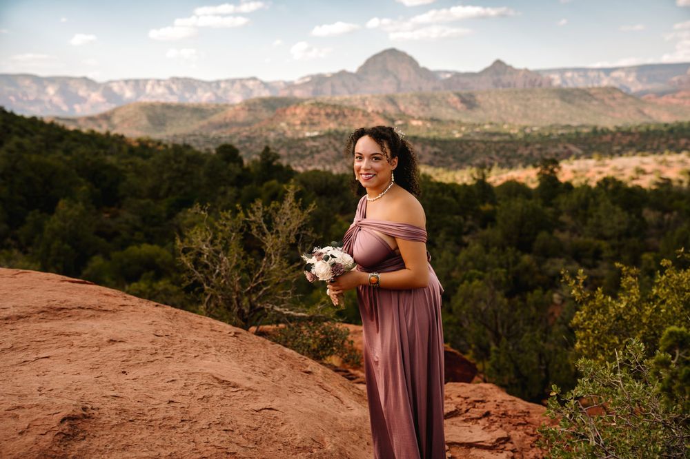 Attendant in mauve dress holds bouquet against backdrop of Sedona's mountain vistas.