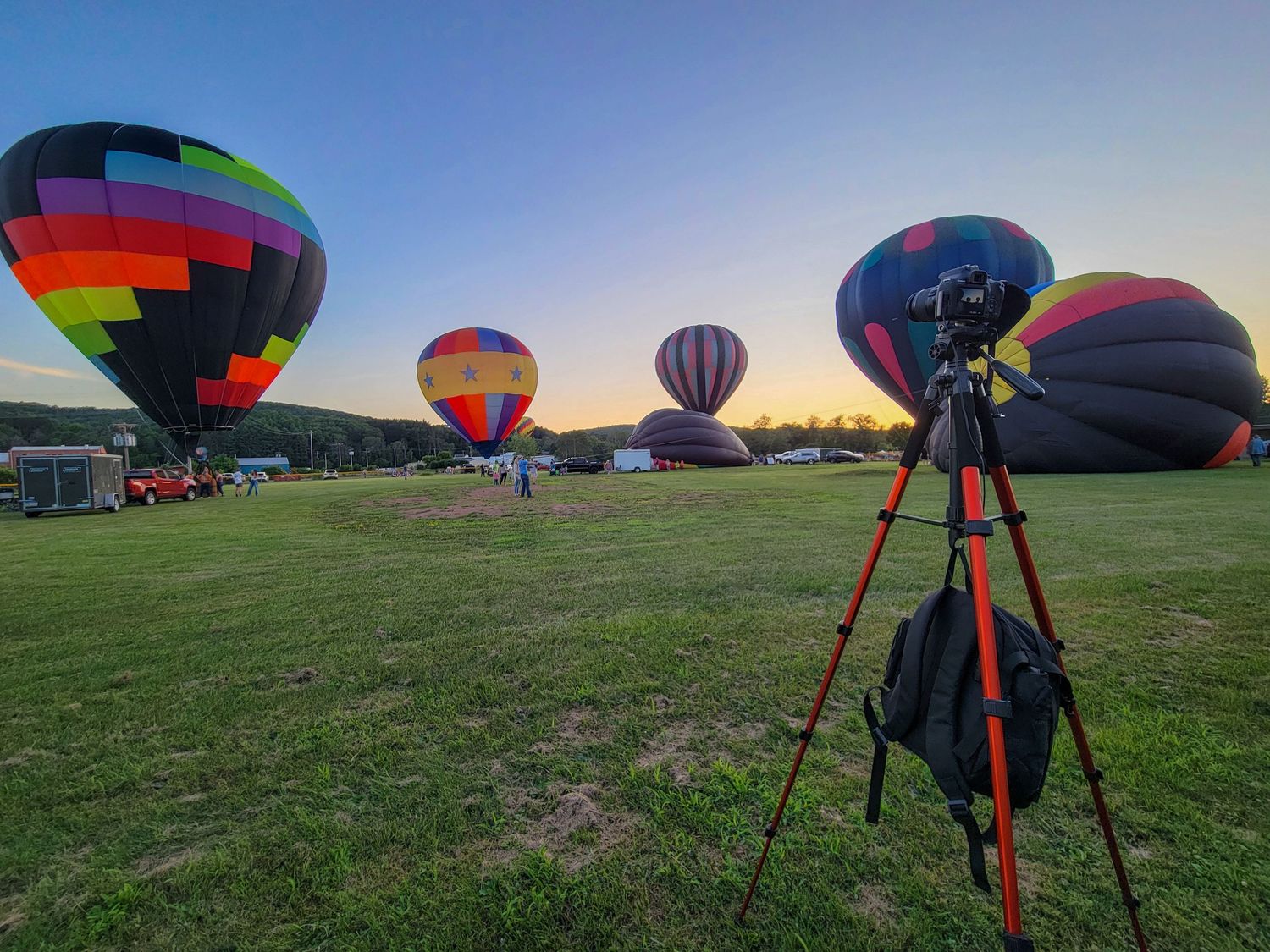 Colorful hot air balloons prepare for takeoff in an open field during sunrise.