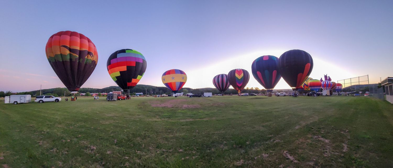 Row of hot air balloons lined up in a field during a balloon festival.
