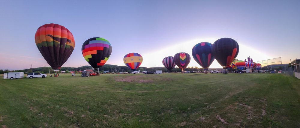 Row of hot air balloons lined up in a field during a balloon festival.