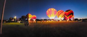 Hot air balloons illuminate the night sky with bright glowing colors.