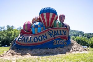 Deflated hot air balloon fabric lies on ground with decorative carnival-style text design.