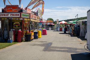 Festival midway with food vendors and concession stands along a paved path.