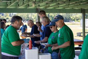People in green shirts serving food under a covered outdoor shelter.