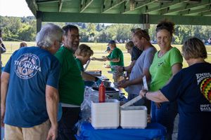 Volunteers and attendees gathering under a green-roofed pavilion during an outdoor event.