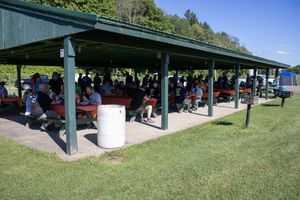 Wide view of a long covered pavilion with people gathered for an outdoor event.