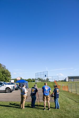 People standing in a line outdoors on a grassy field under bright blue skies.