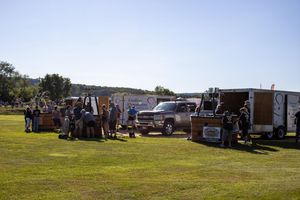 Row of vendor trailers and booths set up on grassy field during outdoor event.