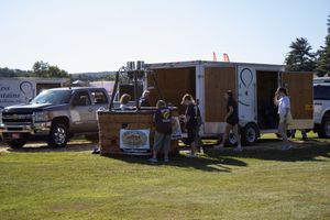 Line of food and vendor trailers parked on grass during community gathering.