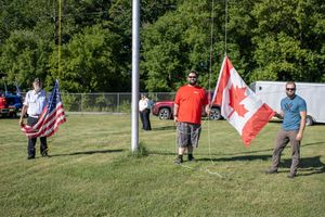 People carrying flags and walking across a green field during ceremony.