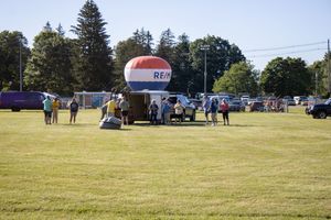 Hot air balloon festival setup area with vehicles and equipment on a sunny grassy field.