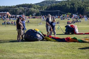Festival attendees gather on a grassy hillside with tents and equipment visible in the background.