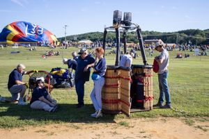 Festival crowd gathers around vendor stands and equipment at a hot air balloon event.