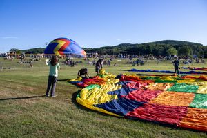Colorful hot air balloon being prepared for flight in a grassy field on a clear blue sky day.