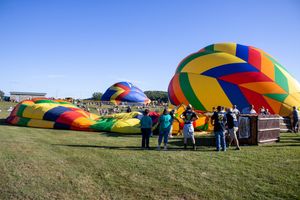 Colorful hot air balloons being inflated on a grassy field against a bright blue sky.