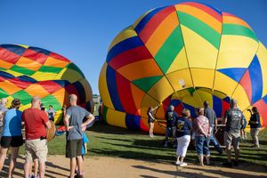 Hot air balloon crew members preparing vibrant balloons for flight at an outdoor festival.