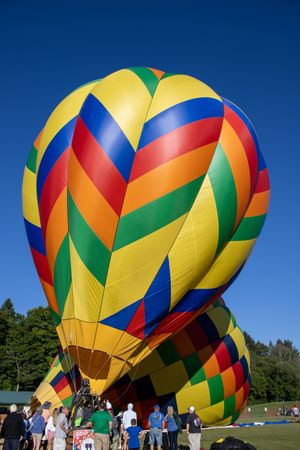 Large yellow and multicolored hot air balloons being inflated with spectators watching.