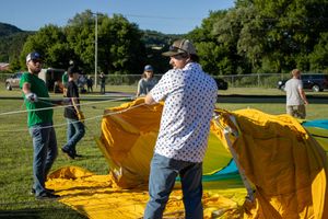 Crew members working together to prepare hot air balloons for launch in a grassy field.