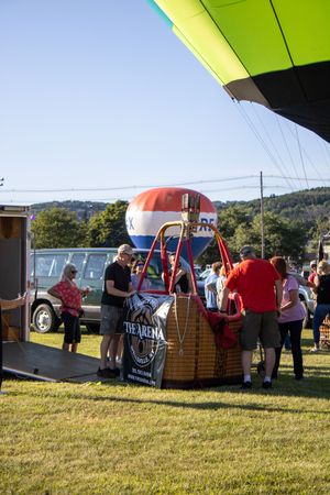 Hot air balloon crews prepare their equipment on a grassy field during a balloon festival.
