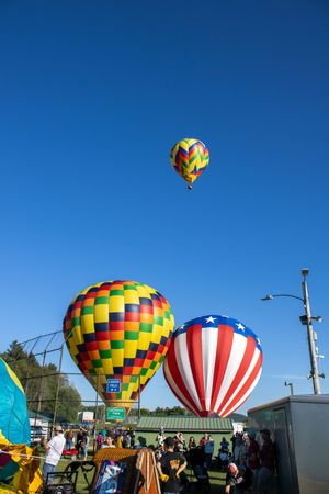 Colorful hot air balloons with patriotic designs rise against a bright blue sky at a festival.