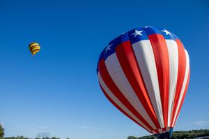 Red, white and blue striped hot air balloons float across a clear blue sky.