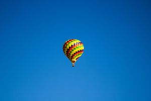 Two hot air balloons with geometric patterns soar through a deep blue sky.