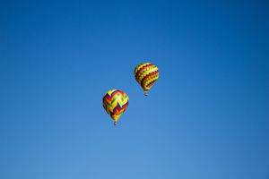 Multiple hot air balloons with checkered patterns drift through the clear blue atmosphere.
