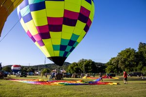 Colorful hot air balloons being inflated on a grassy field against a bright blue sky during a balloon festival.