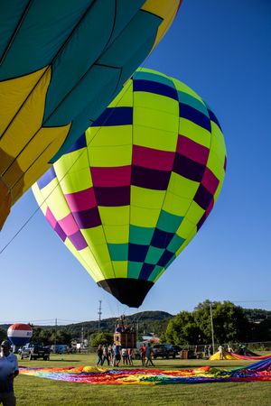 A neon yellow and pink checkered hot air balloon being inflated on a sunny day.