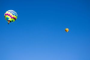 Multiple hot air balloons floating in a vivid blue sky during a balloon festival.