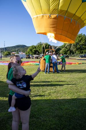 A large yellow hot air balloon being prepared for launch with spectators gathered on the grass.