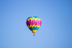 Hot air balloons with vibrant patterns soar in a clear blue sky.