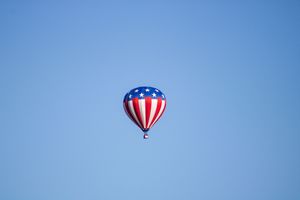 Red, white and blue patriotic hot air balloons drift through the air.