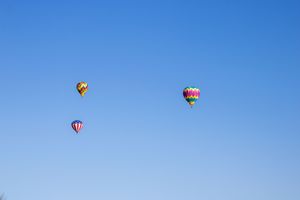 Multiple hot air balloons ascending into a pristine blue sky.