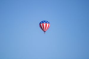 Patriotic themed hot air balloon soaring through clear blue skies.