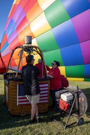 Colorful striped hot air balloon being prepared for launch with crew.