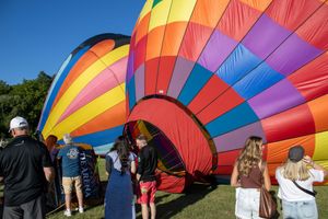 Hot air balloon crews prepare colorful balloons for launch at a festival on a sunny day.