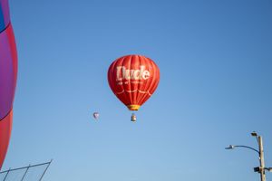 Red hot air balloon rising against bright blue sky with others in distance.