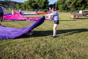 Ground crew members work together to spread out a large purple hot air balloon envelope.