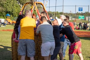 Spectators gather around a hot air balloon basket during a festival setup.