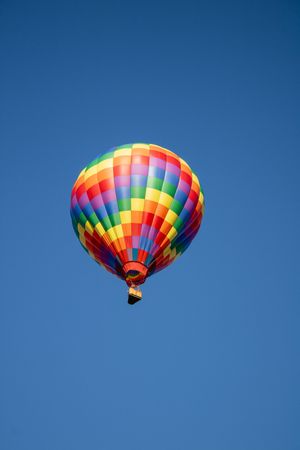 A rainbow-colored hot air balloon soars through a pristine blue sky.