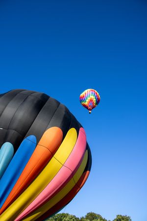 Colorful hot air balloon with black, orange, yellow and pink stripes floating against bright blue sky.