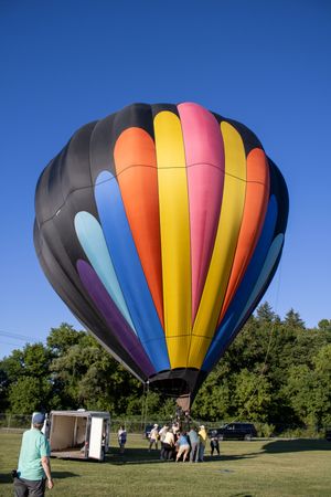 Ground crew preparing a vibrant striped hot air balloon for launch in a grassy field.
