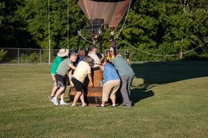 People gathering around equipment on a grassy field during a hot air balloon setup.
