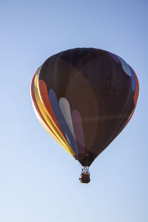 Dark hot air balloon with orange and red accents silhouetted against bright blue sky.